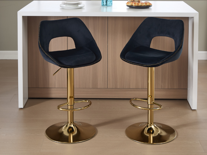 Modernes Interieur mit vier schwarz gepolsterten Barhockern mit Metallfüßen aus Gold/Messing, die in einer Reihe auf einem neutralen beigen Boden angeordnet sind.