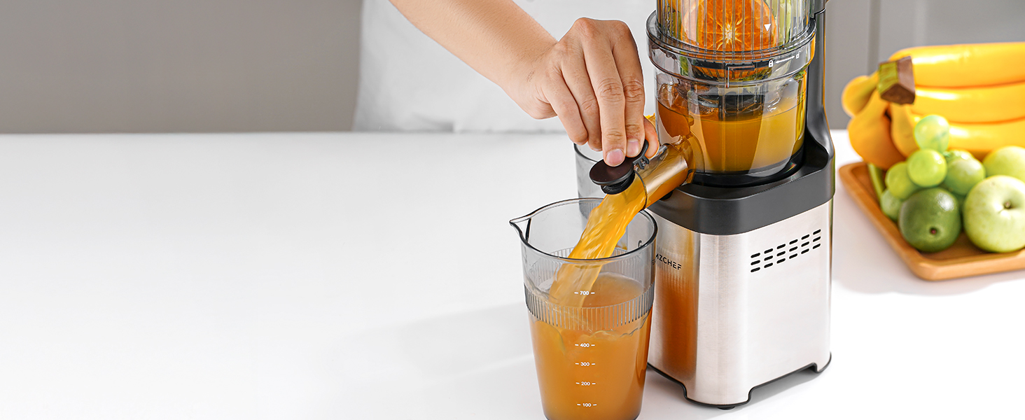 Moderne Saftpresse mit Edelstahloberfläche, die Orangensaft in ein Glas gießt, im Hintergrund sind frische Früchte sichtbar
