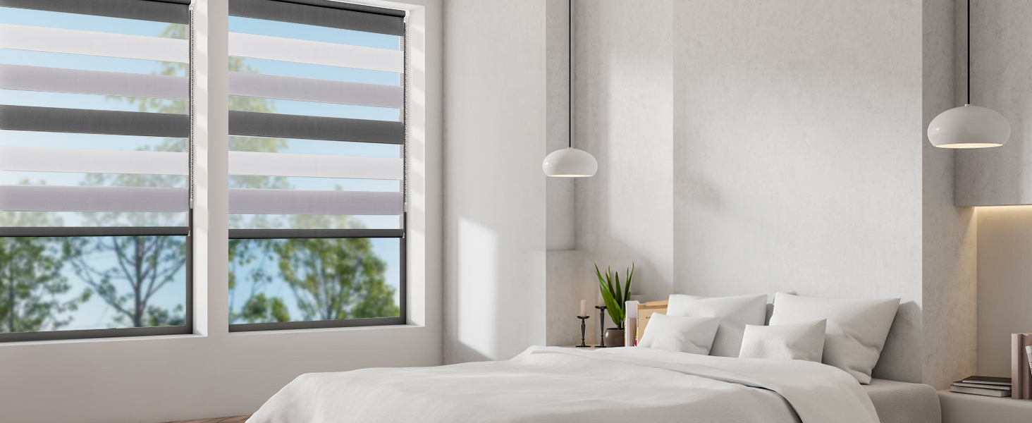 Chambre lumineuse et minimaliste avec de grandes fenêtres, des murs blancs et des suspensions. Lit avec literie de couleur claire visible au premier plan