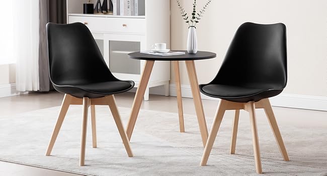 Modern dining set with round wooden table and two black chairs featuring molded seats and wooden legs. Clean, minimalist design suitable for small spaces.