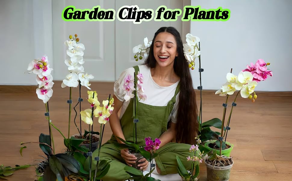 Garden clips for plants displayed with various potted orchids. A woman in green overalls sits smiling among colorful flowering plants on a wooden floor.