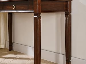Gros plan d'un pied de console en bois et d'un tiroir. Finition marron foncé avec détails sculptés ornés sur la jambe. Vue partielle d'un tiroir unique avec bouton métallique.