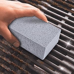 Tenez à la main un bloc de nettoyage gris et poreux sur des grilles rouillées. Le bloc est utilisé pour frotter et nettoyer les barres métalliques du gril.