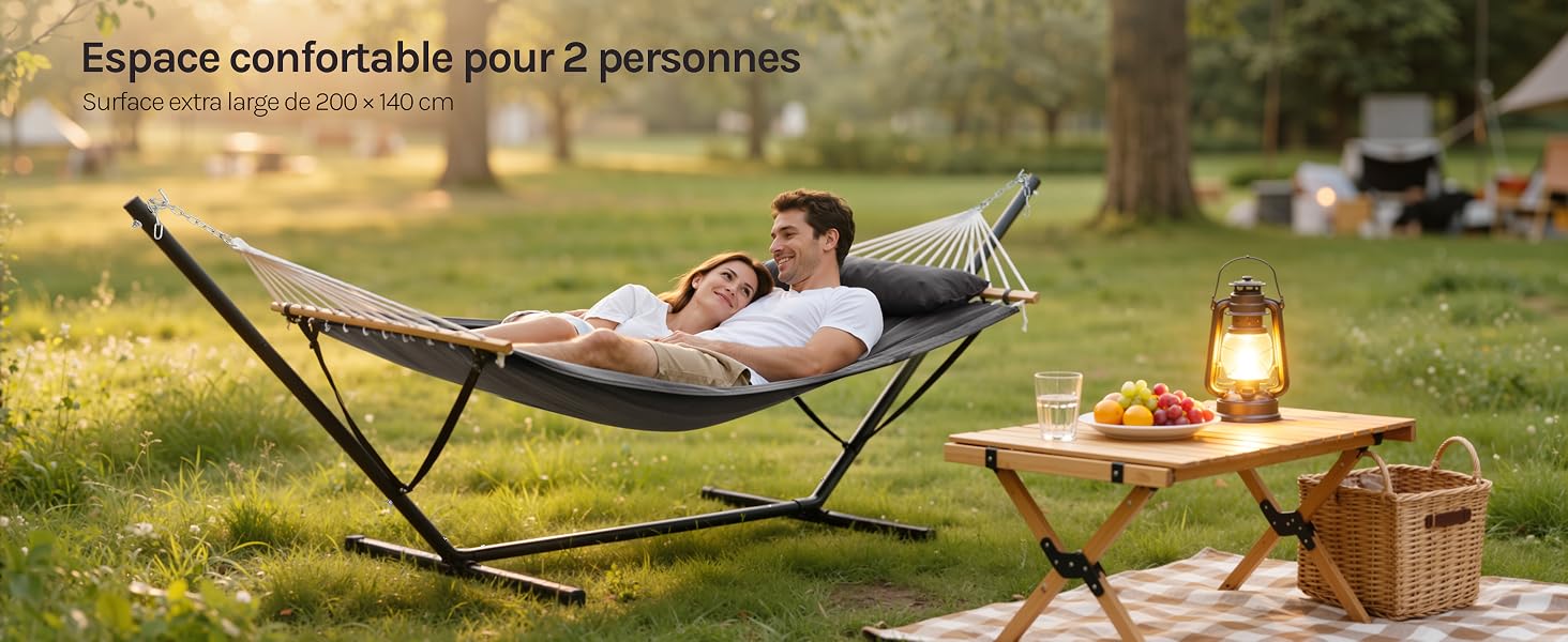 Scène de détente en plein air avec chaise de camping pliante et installation de pique-nique sur l'herbe. Lanterne et produits alimentaires visibles sur une couverture en milieu naturel.
