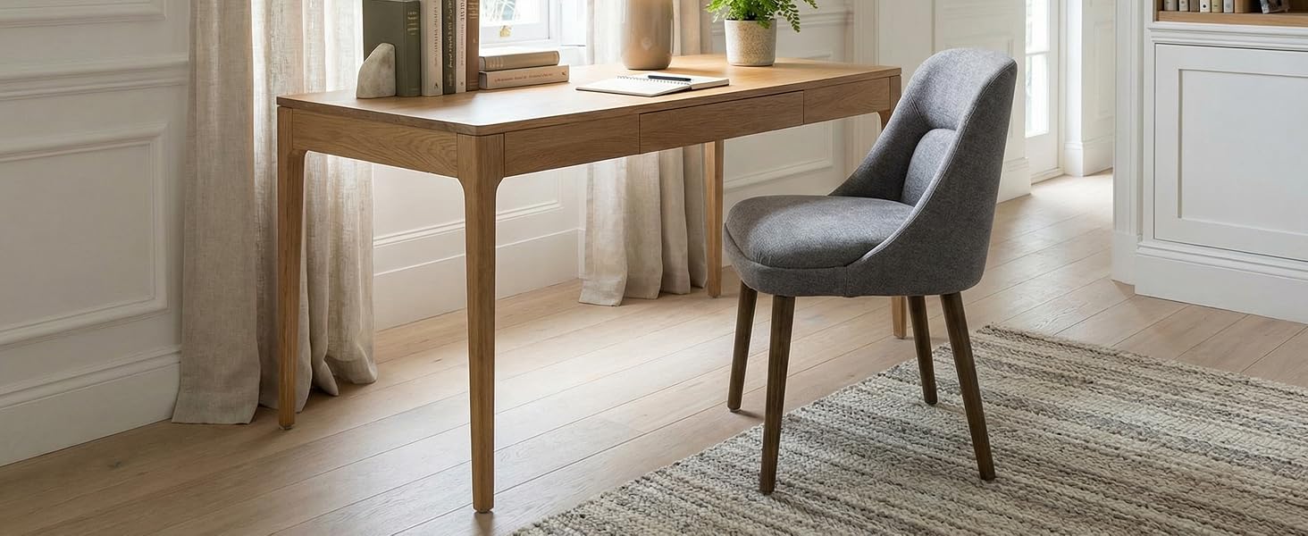 Elegant wooden desk with tapered legs paired with upholstered gray dining chair on natural fiber area rug in bright interior setting.