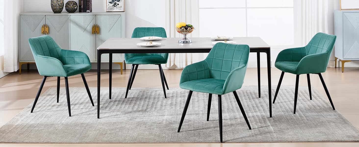 con una mesa redonda con patas negras y sillas tapizadas en verde azulado. Ubicado en un espacio interior luminoso y minimalista.