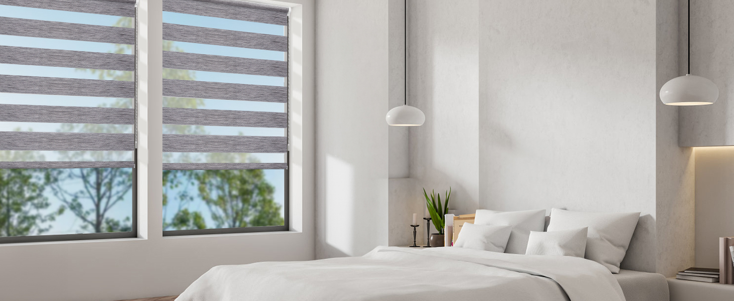 Chambre lumineuse avec literie blanche, stores de style zèbre, lampes suspendues et plante en pot sur la table de chevet. Les grandes fenêtres offrent une vue sur l'extérieur.