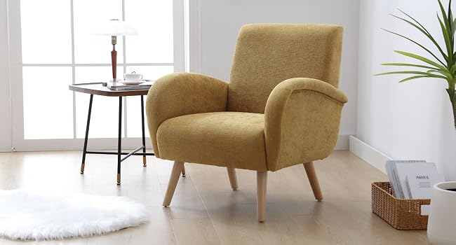 Mid-century style armchair with mustard yellow upholstery, curved arms, and wooden legs. Placed in a bright room with a side table and decorative elements.