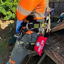 Gros plan de la ceinture à outils et du harnais d'un ouvrier des services publics avec des vêtements orange à haute visibilité et un équipement de sécurité attaché, y compris une pochette de premiers soins rouge