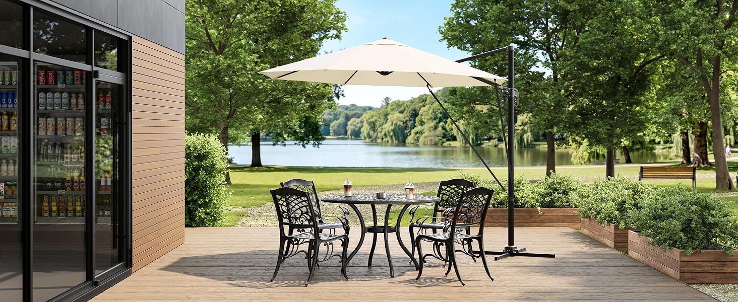 Terrasse extérieure avec bâtiment en brique, avec des tables et des chaises en métal sous des parasols. Des jardins paysagers et des arbres visibles en arrière-plan.