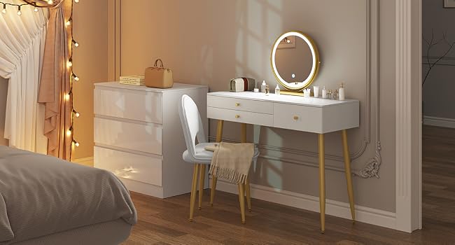 White bedroom vanity with illuminated mirror, drawers, and chair. String lights on curtains and dresser visible in background.