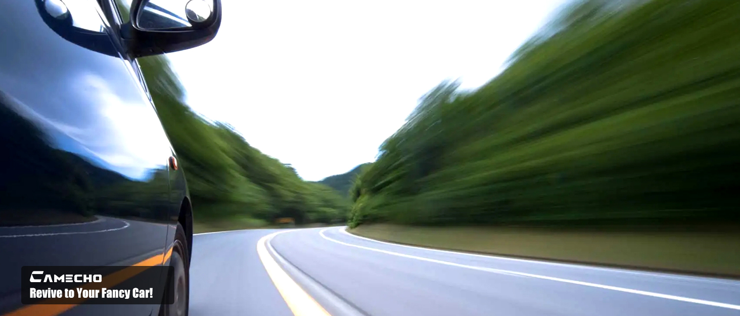 Dashboard view through car windshield of curving mountain road with motion blur effect. Lush green mountain slopes visible on both sides. 'CARCCHO' watermark visible in corner.