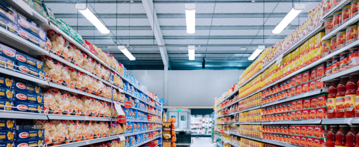 Innenansicht eines Supermarktgangs mit Regalen, die mit verschiedenen verpackten Lebensmitteln bestückt sind. Helles fluoreszierendes Licht beleuchtet die Szene.