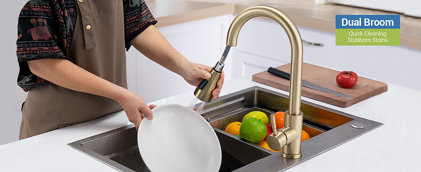Gold-finished pull-down kitchen faucet with dual spray function being demonstrated over stainless steel sink with fruits visible.