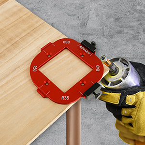 Red circular router template guide mounted on wooden surface, with gloved hand holding measuring tool against its edge.