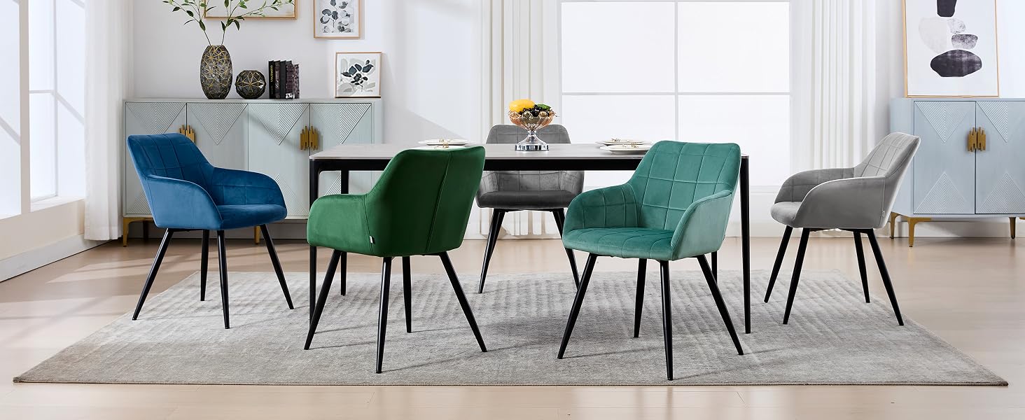 con mesa ovalada negra con seis sillas tapizadas en azul, verde y gris. Colocado sobre una alfombra de color claro en una habitación luminosa y minimalista