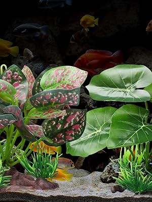 Aquarium setup with artificial plants including pink-spotted and solid green leaves, decorative aquatic vegetation on sandy substrate with tropical fish swimming.