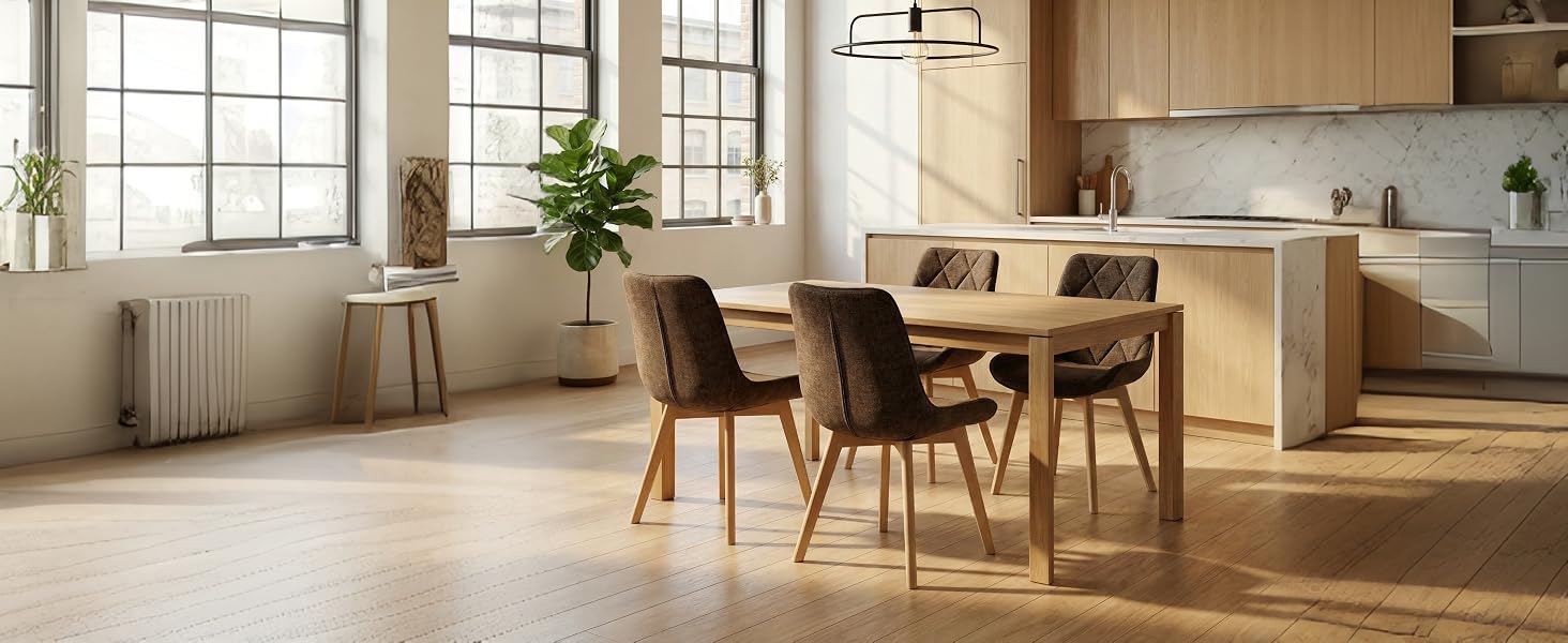 Intérieur de la salle à manger moderne comprenant une table à manger en bois clair avec quatre chaises brunes rembourrées, une cuisine ouverte visible, de grandes fenêtres avec éclairage naturel, un décor minimaliste.