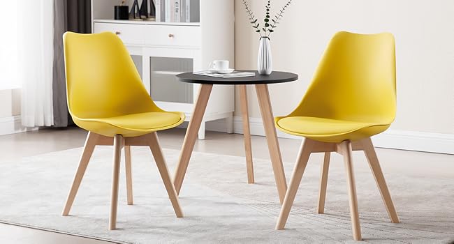 Two yellow modern dining chairs with wooden legs, paired with a small round table with wooden legs in a bright interior setting.