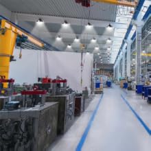 Moderne industrielle Produktionsstätte mit heller Deckenbeleuchtung, blauen Bodenmarkierungen und verschiedenen Maschinen und Geräten entlang der Produktionslinie