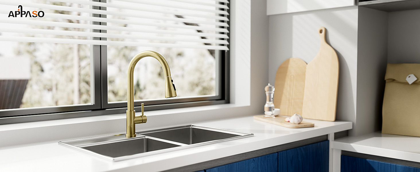 Modern kitchen sink with gold pull-down faucet, installed in white countertop near window. Features minimalist design and contemporary styling.