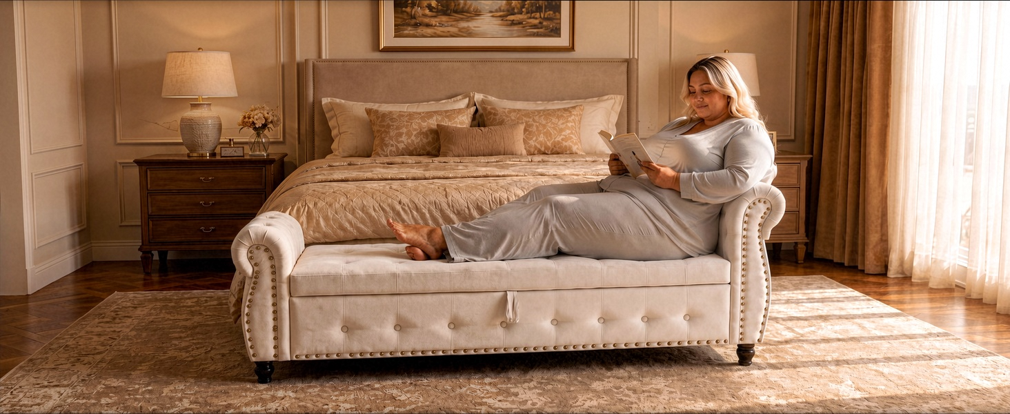 Woman seated on cream-colored upholstered sofa with rolled arms in warm wood-paneled bedroom with side table and lamp.