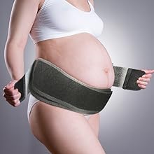 Pregnant woman wearing a white top and applying a dark-colored support belt around her lower abdomen.