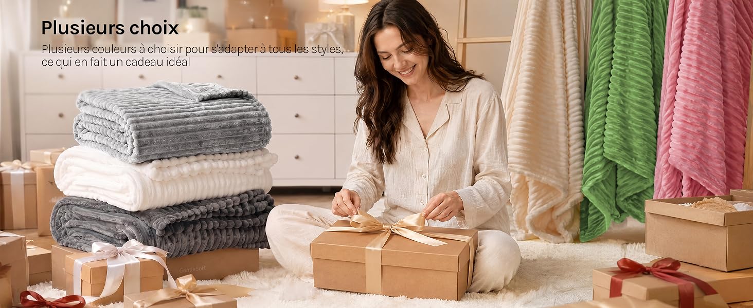 Femme portant un haut sans manches bleu clair, assise et enveloppant du papier kraft autour de cadeaux emballés, avec des chandails empilés et des foulards colorés visibles sur des étagères derrière elle à la maison.