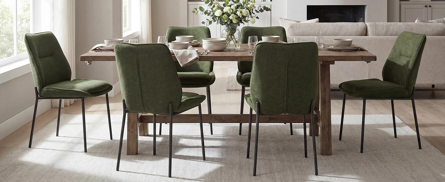 Interno moderno della sala da pranzo con tavolo rotondo, quattro sedie verdi imbottite e arredamento minimalista in uno spazio luminoso e pulito.
