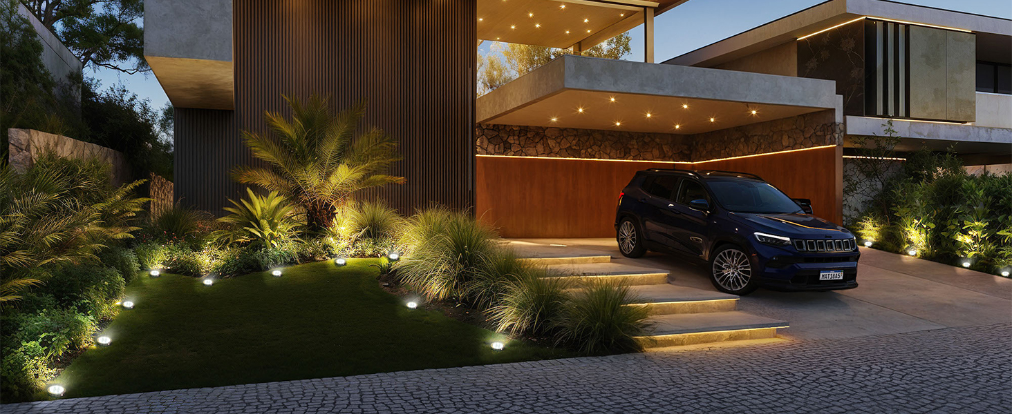 Extérieur de maison moderne au crépuscule avec éclairage paysager illuminant les plantes et la passerelle, avec un véhicule garé dans la zone d'abri d'