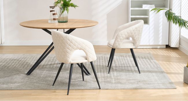 Ensemble de salle à manger moderne avec table ronde en bois et deux chaises rembourrées crème avec pieds en métal noir, posées sur un tapis gris.