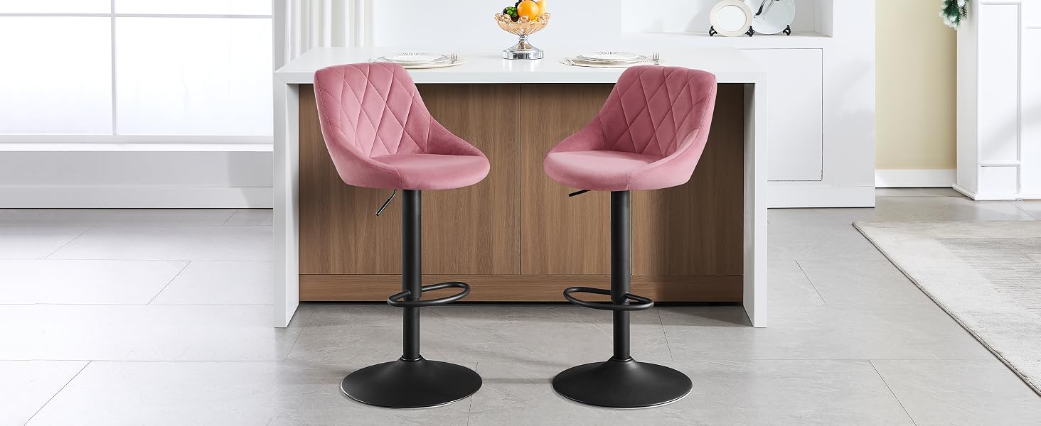 Due sgabelli da bar in velluto rosa con schienali trapuntati e basi circolari nere, posizionati su un'isola da cucina bianca con accenti in legno