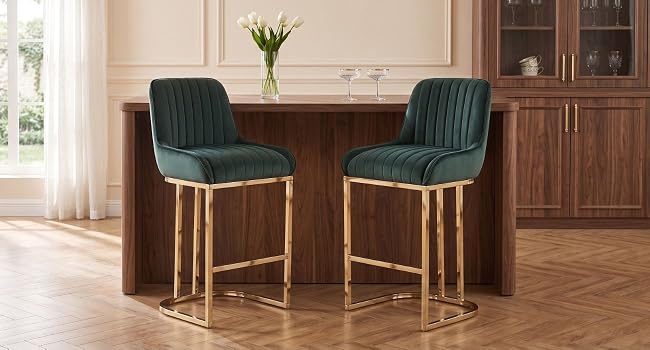 Paire de tabourets de bar modernes avec sièges rembourrés bleu sarcelle, pieds en métal doré, placés sur un comptoir en bois dans un cadre intérieur chaleureux avec des plantes et des armoires en bois.