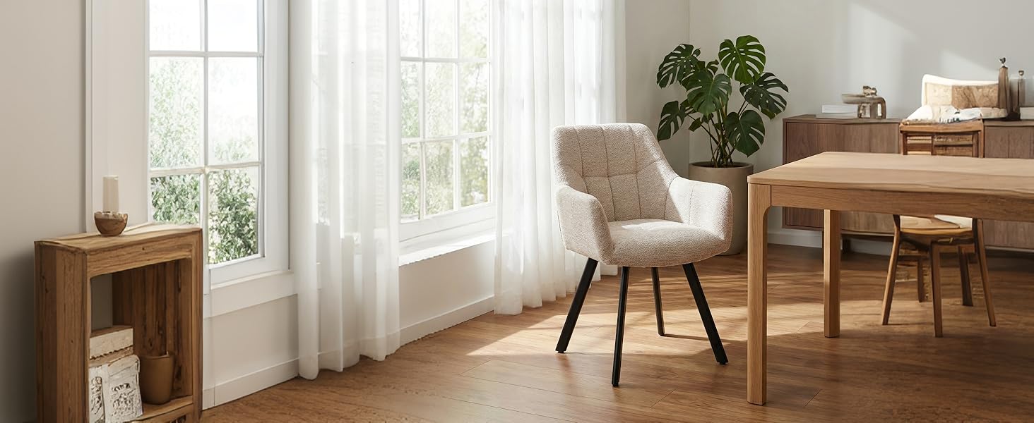 L'intérieur du salon moderne comprend des meubles en bois, notamment une table à manger avec des chaises, une étagère en bois, des plantes en pot et des fenêtres du sol au plafond avec des rideaux blancs laissant entrer la lumière naturelle.