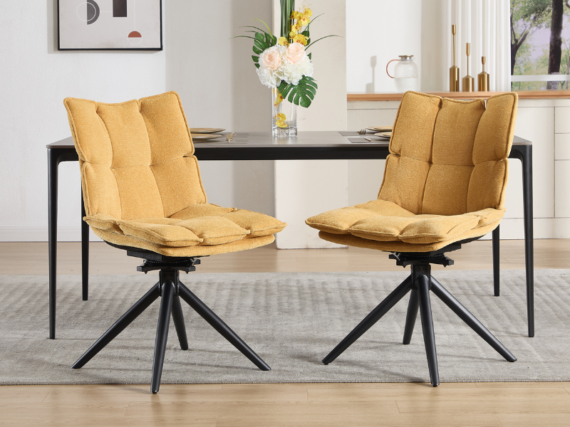 Dos sillas de comedor capitonadas de color amarillo mostaza con modernas bases giratorias de metal negro, colocadas en una mesa de comedor oscura en un ambiente interior contemporáneo.