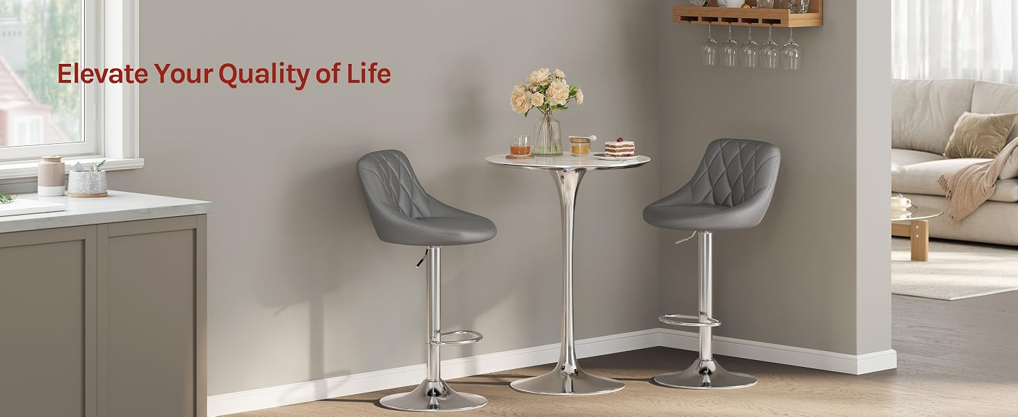 Text reads 'Elevate Your Quality of Life'. Interior scene featuring two gray upholstered chairs with metal legs flanking a round side table in a modern living room with neutral decor.