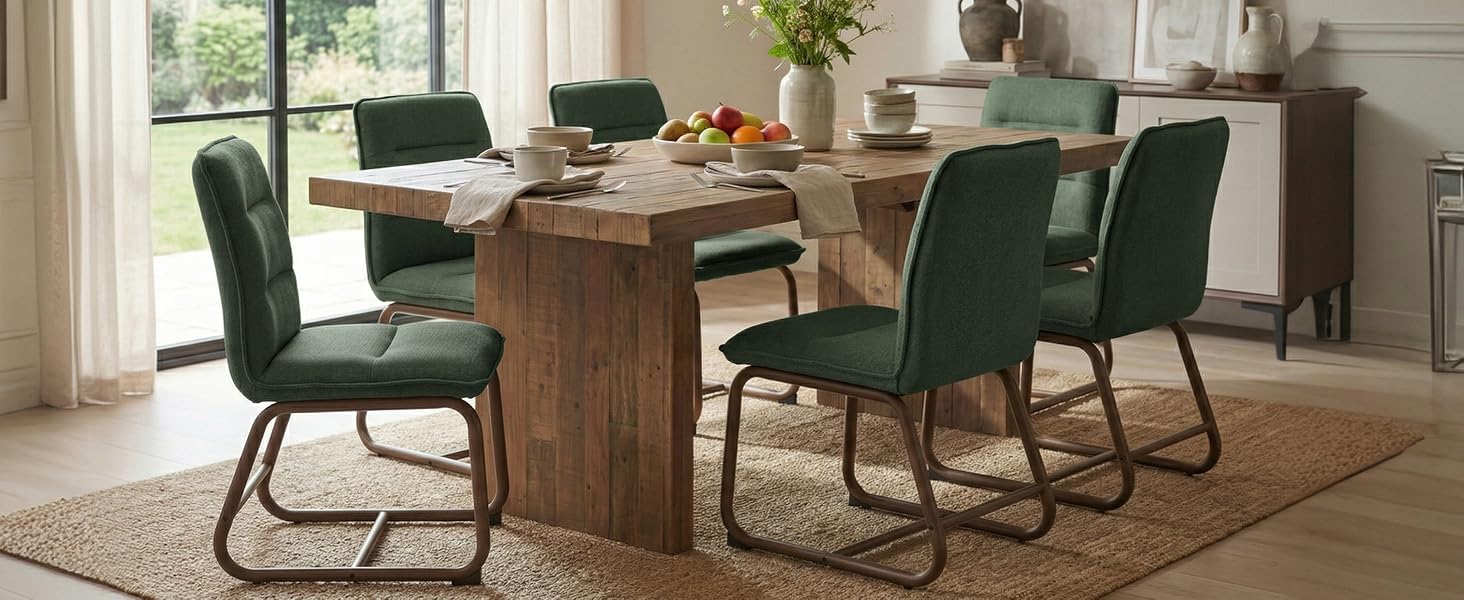 Modern dining room setting with emerald green velvet cantilever chairs arranged around a wooden dining table in a bright, contemporary space.
