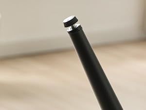 Stylo ou stylet cylindrique noir avec bande métallique argentée près de la pointe, photographié sur fond beige neutre.
