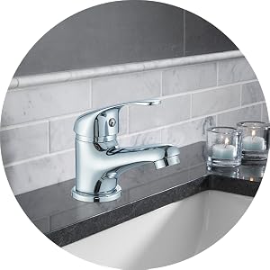 Chrome bathroom faucet mounted on gray tile wall above dark counter, with decorative glass containers visible.