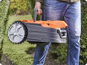 Tosaerba robotizzato arancione e grigio utilizzato all'aperto sull'erba, con solo il dispositivo e le gambe dell'operatore visibili.