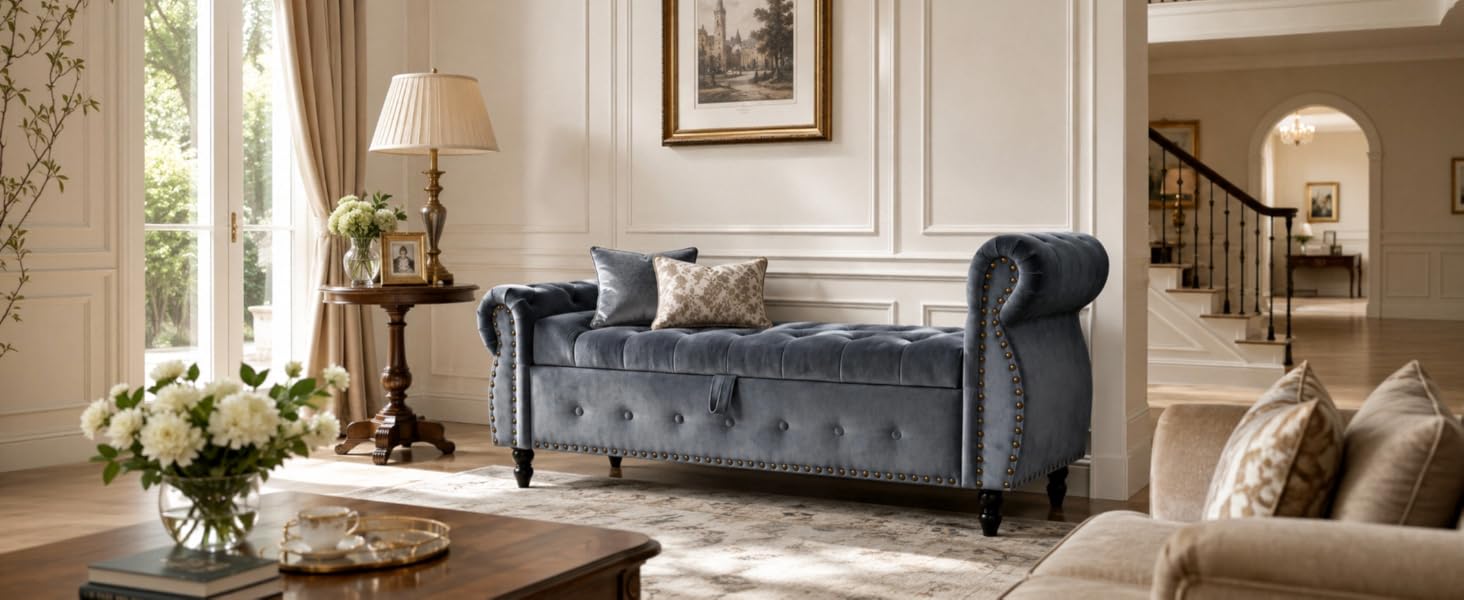 Navy blue tufted velvet chesterfield-style bench sofa with rolled arms and nailhead trim in elegant classical living room interior. Piece positioned under artwork with coordinating home décor including side table, floor lamp, fireplace, and traditional furnishings.