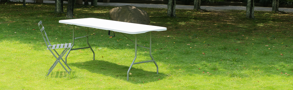 Cadre extérieur montrant des chaises pliantes en métal blanc et une table sur une pelouse verte.