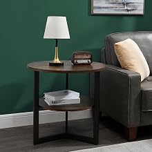 Runder Beistelltisch mit zweistöckiger Holzplatte und schwarzen Metallbeinen, der neben einem grauen Sofa steht. Auf dem Tisch stehen eine Lampe und kleine Dekorationsgegenstände