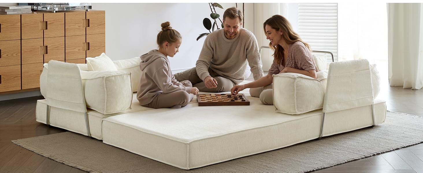 Tres adultos sentados en un gran sofá modular seccional de color crema sobre piso de madera con juguetes para niños y contenedores de almacenamiento cerca.