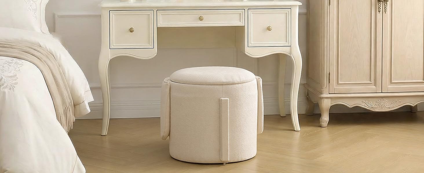 Interior room setting with cream-colored furniture, featuring white console tables and a round upholstered ottoman on light wooden flooring.