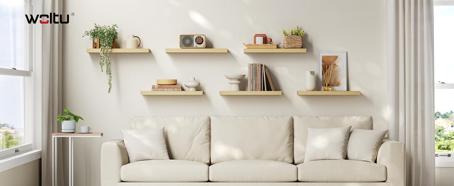 Intérieur du salon avec canapé beige contre mur blanc décoré d'étagères flottantes en bois. Plantes et objets de décoration disposés sur des étagères au-dessus du canapé.
