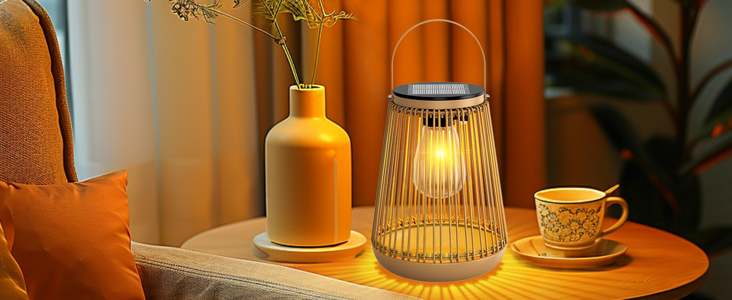 Scène de décoration intérieure confortable comprenant une lanterne en fil de fer avec une lumière rougeoyante, un vase en céramique jaune avec des fleurs séchées et une tasse de thé décorative sur une surface en bois. Coussin orange visible en arrière-plan.