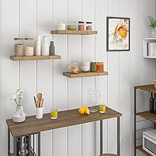 Rustic wooden floating shelves mounted on white shiplap wall, displaying kitchen storage containers, utensils, and decorative items with framed artwork.