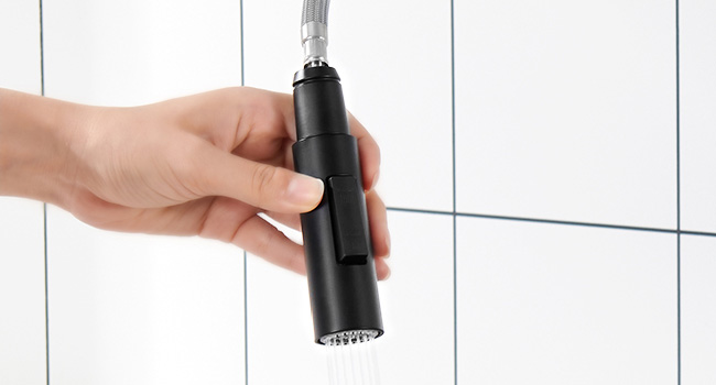 Holding a black handheld shower head against a white tiled background, demonstrating its compact size and ease of use.