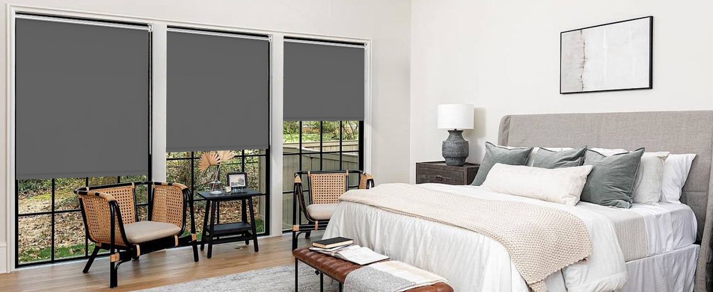 Intérieur de chambre moderne avec volets roulants gris, lit blanc avec oreillers gris et décoration minimaliste sur des murs blancs.